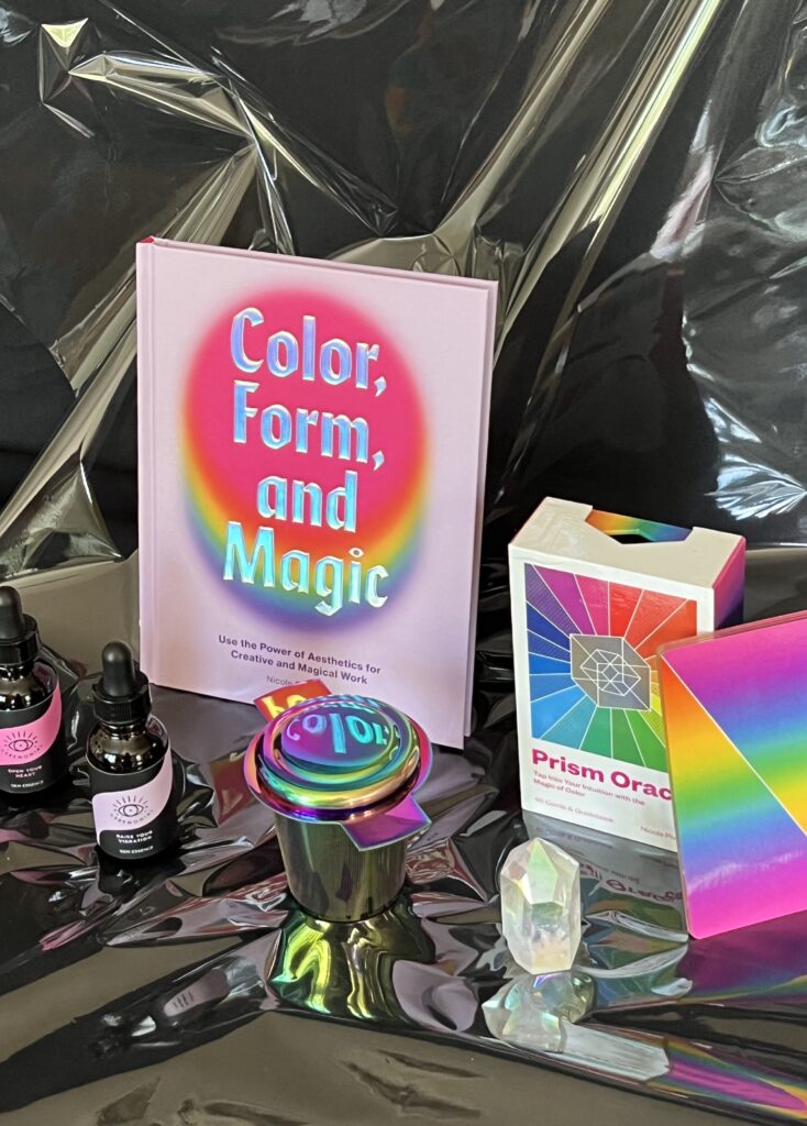 Various colorful witchy supplies such as books, tarot cards, and crystals sit out on a black tablecloth.