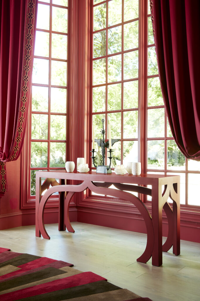 A room with large windows is painted red with red curtains and a red table in front of the windows.