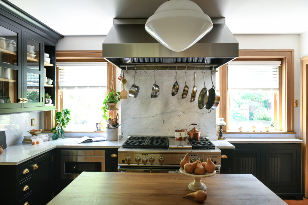 A kitchen remodel with ladles hanging above the stove range, a wooden table in the middle, white counter tops, and black cabinets.