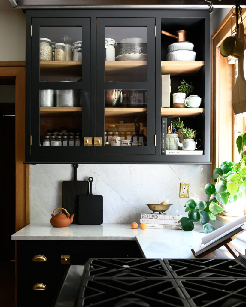 Black kitchen cabinets above and below a white counter top with black cutting boards leaning against the white backsplash.