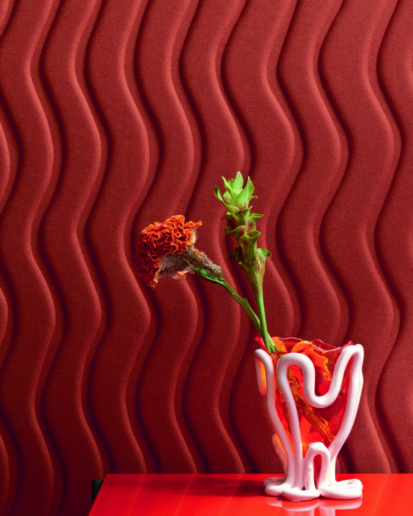 A red wavy wall with a vase in front of it on a red table.