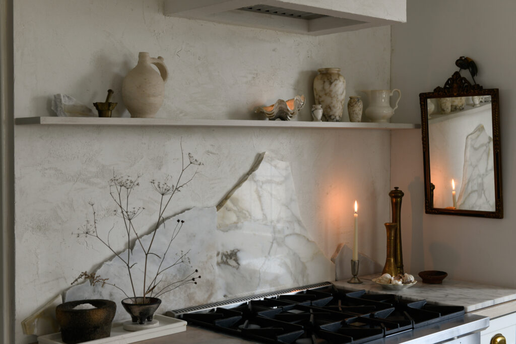On top of Erin Kelly's white countertop against the back wall sits a broken stone countertop surrounded by plants, candles, and other knickknacks. 