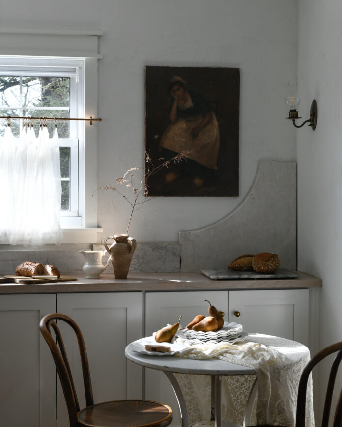 In Erin Kelly's white kitchen sits a small table with two chairs and a slab of broken stone countertop on top of the regular counter.