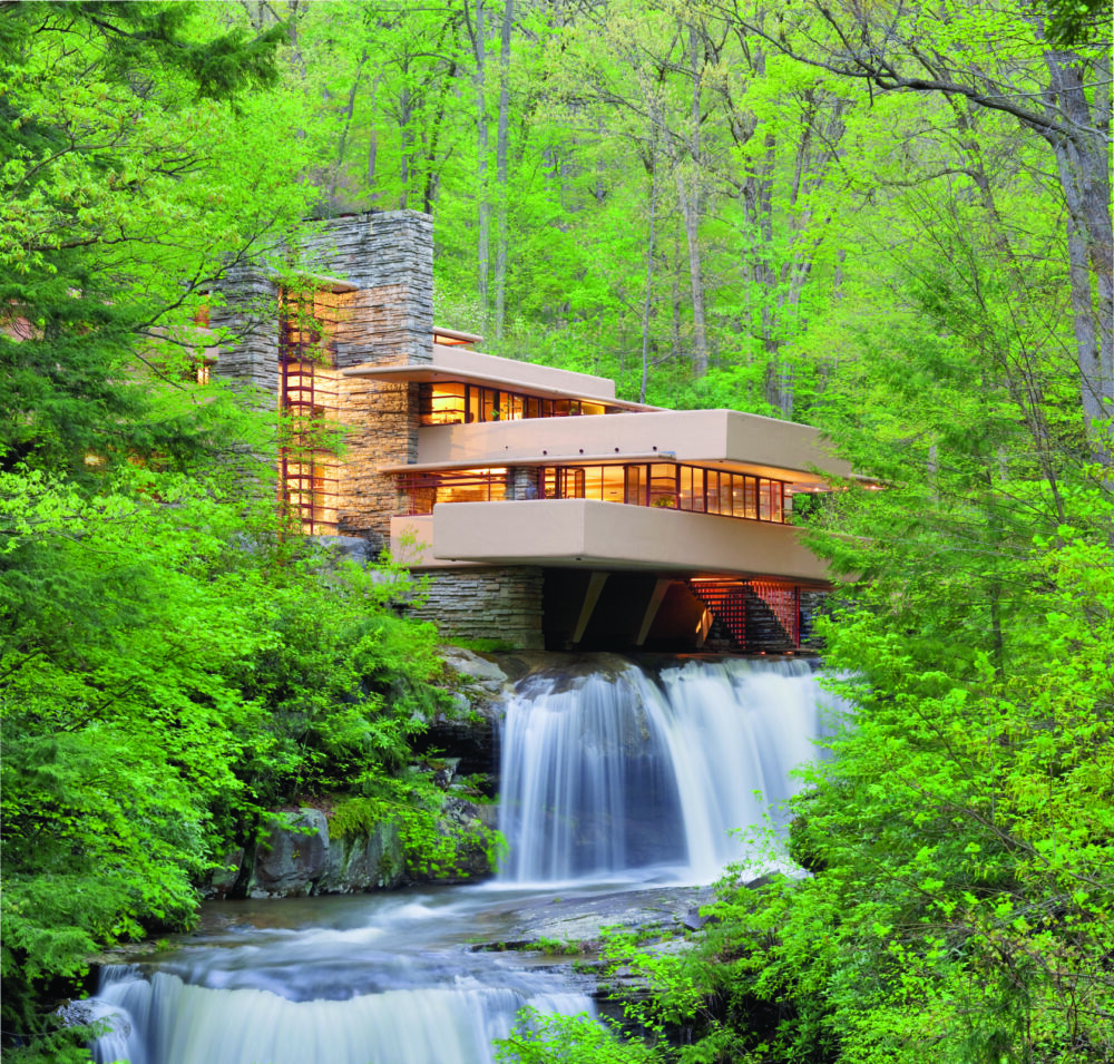 A photo of Fallingwater nestled in a lush green wooded area with the waterfall and stream running through it.