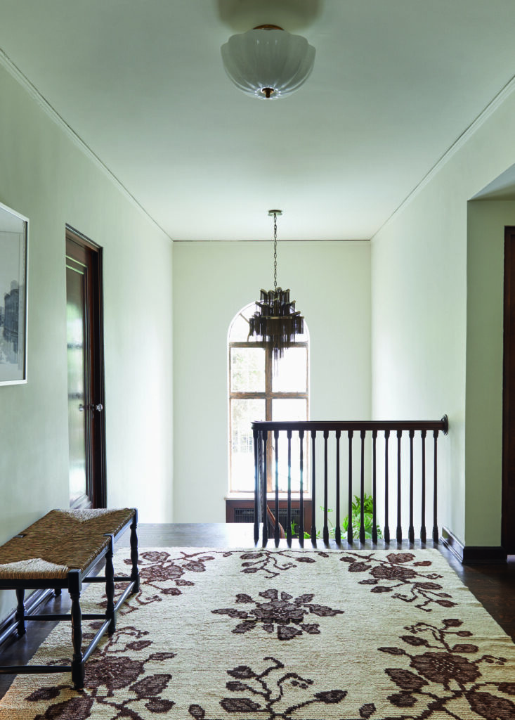 An entry way before bedrooms with a beige carpet with roses on it and a chandelier by Studio Lithe.
