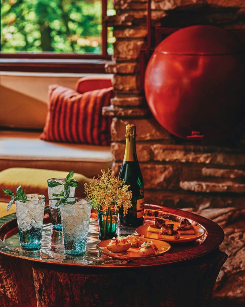 A cocktail table holds three blue cocktails and a plate of potato halves topped with pickled ramps.