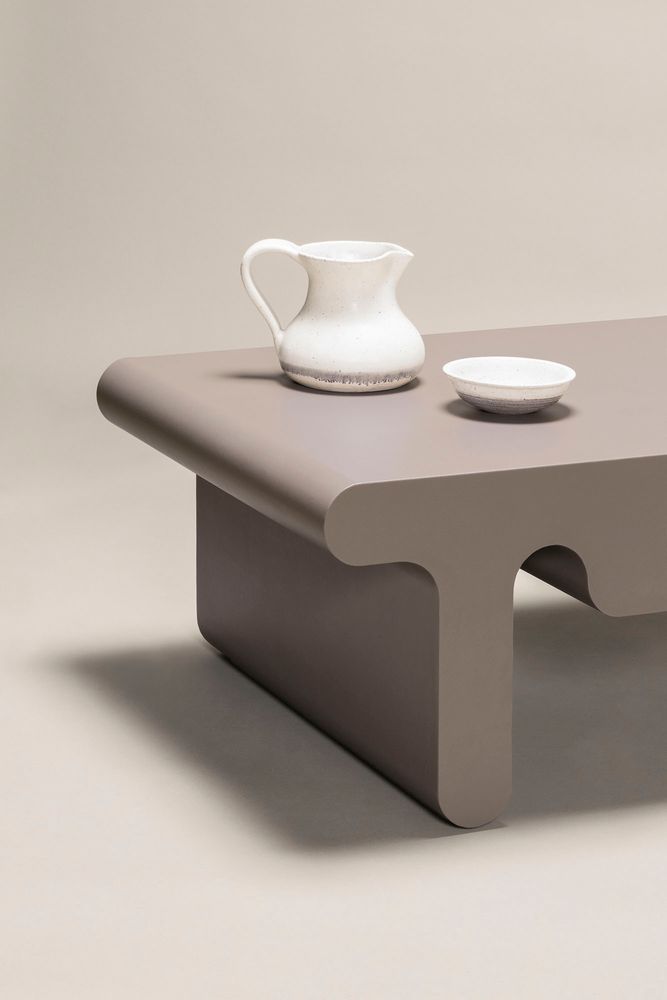 A neutral grey table on a beige backdrop with two white glass pieces on top of it.