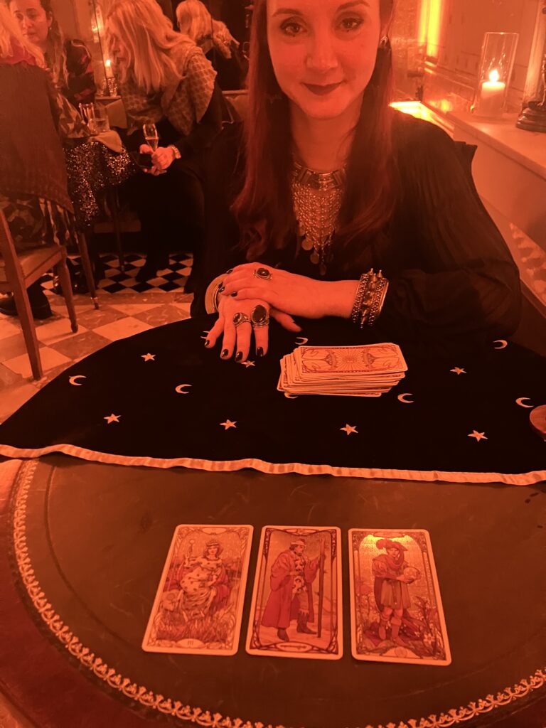 A woman gives a tarot reading with three cards in front of her as red lighting lights up Paris Design Week.