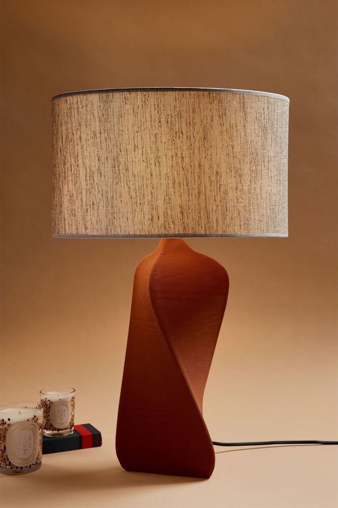 An orange lamp sits against a light brown wall on a table.