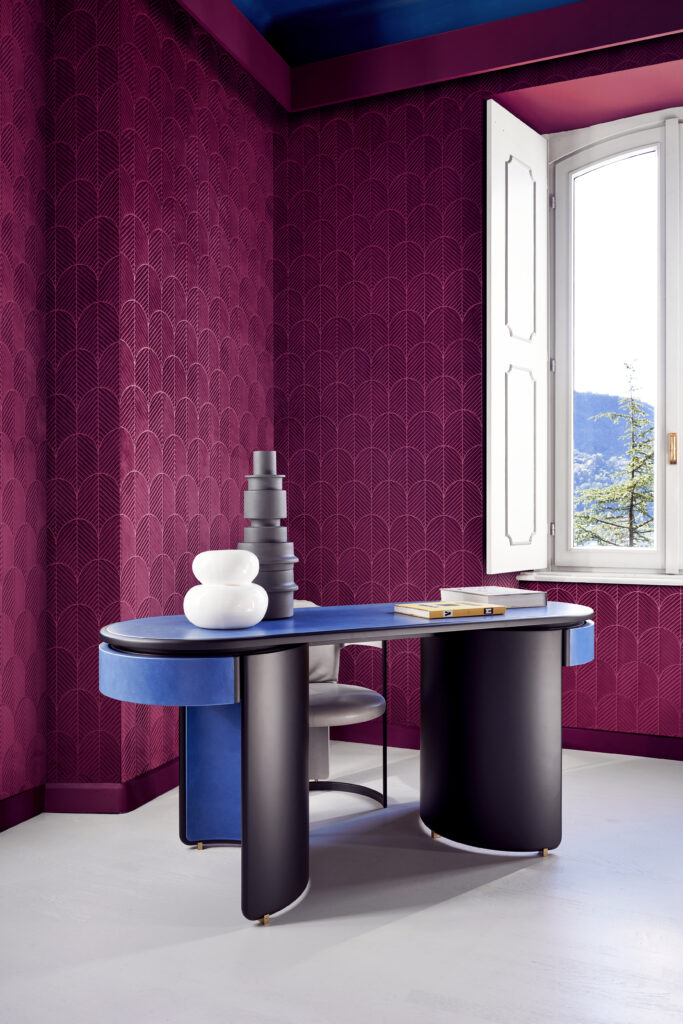 A work room with burgundy walls and a blue desk in the middle of the room.
