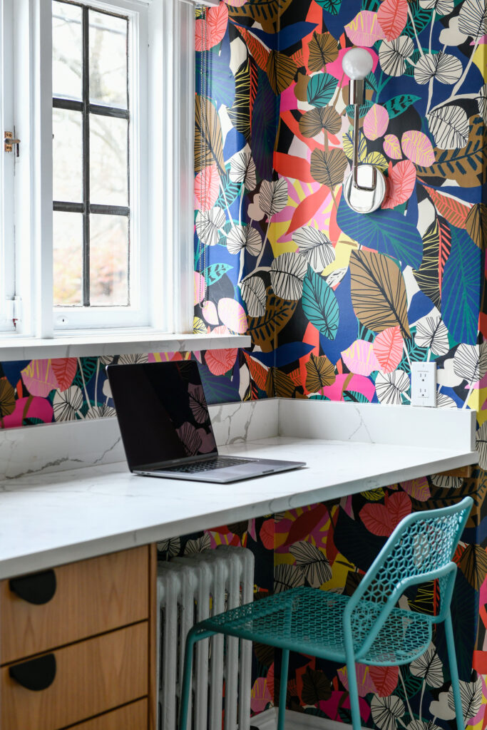 A white marble desk holds a laptop with colorful leaf wallpaper and a blue chair.