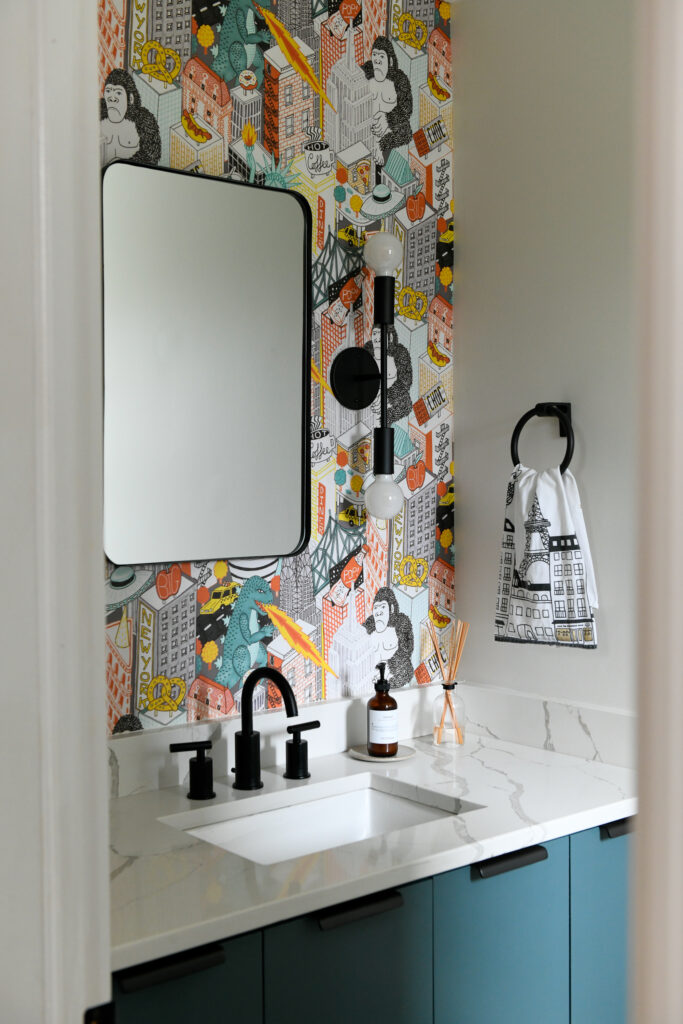 A bathroom mirror and black sink with marble countertops and flashy cartoon building and character wallpaper.