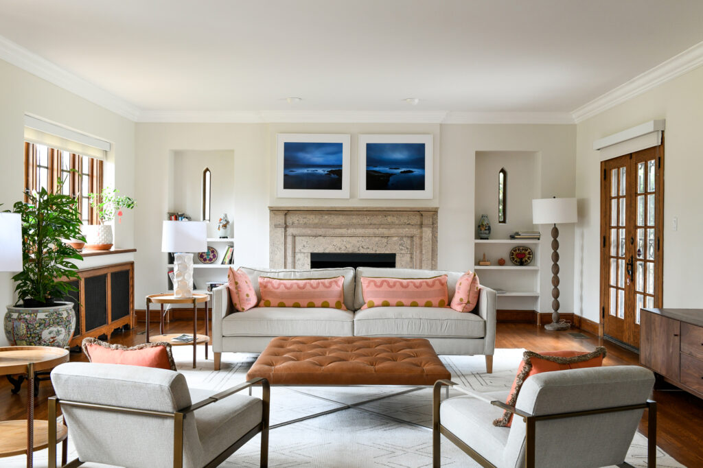 A living room setting with grey couches and chairs, pink pillows, and white walls throughout. 