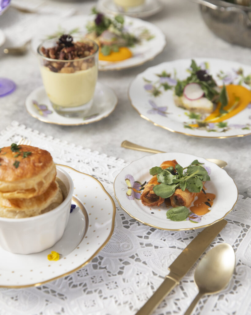 Small white plates of salads and parfaits sit on a white table accompanied by light gold silverware and other embellishments.