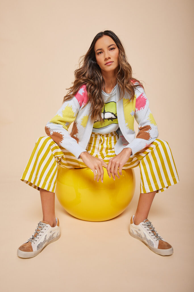 A woman in bright patterned clothing sits on a yellow ball