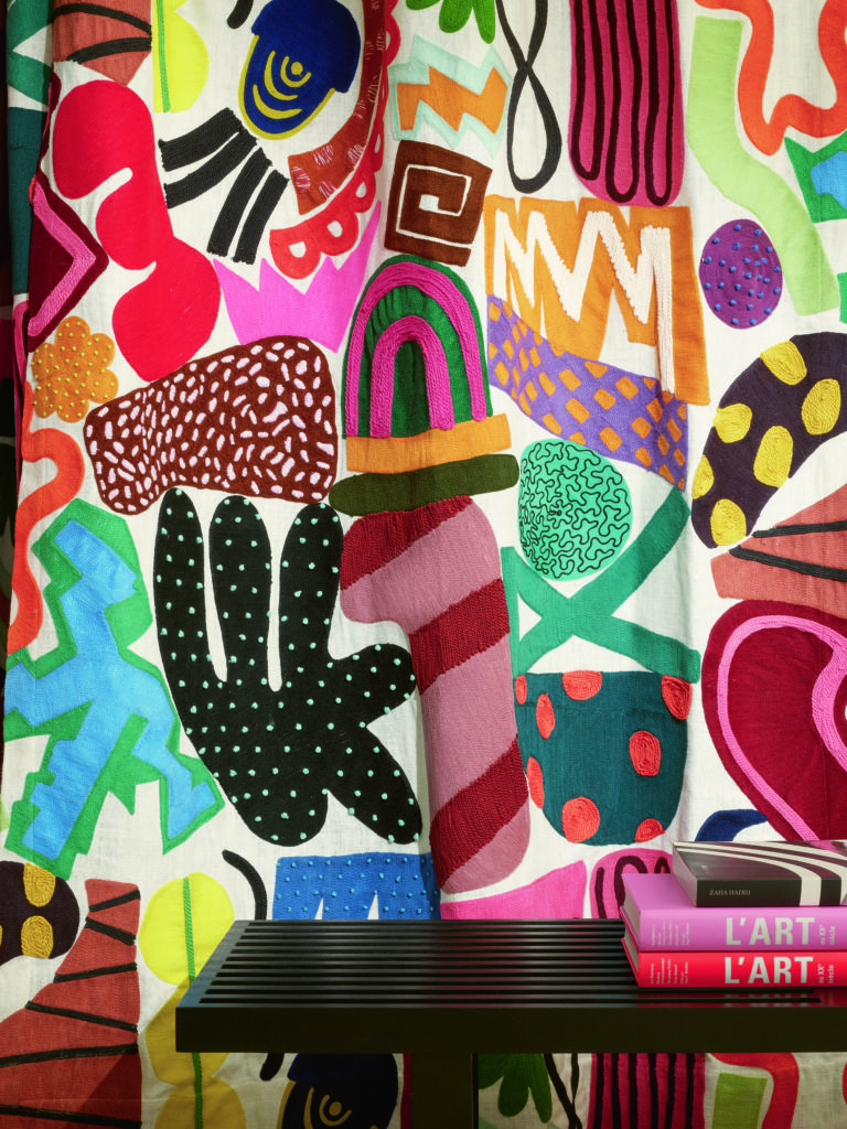 A graffiti style wall in dark colored with a dark table in front of it that has three pick books sitting on it. 