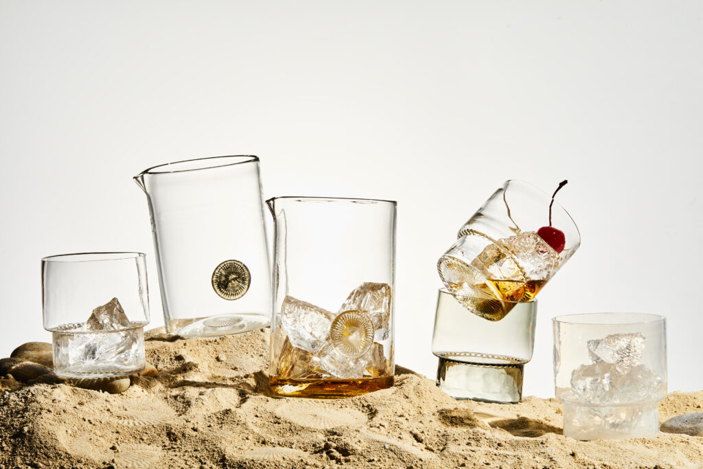 Five glasses from Pittsburgh glassworks on top of sand.