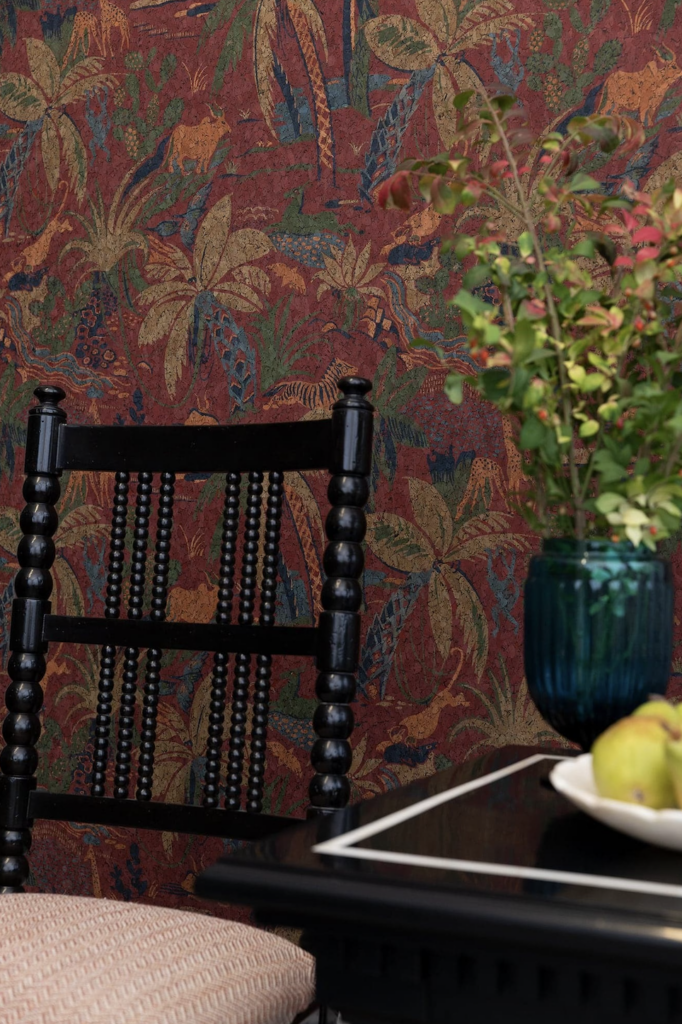 A dark red flower textured wallpaper sits behind a black chair and black table.