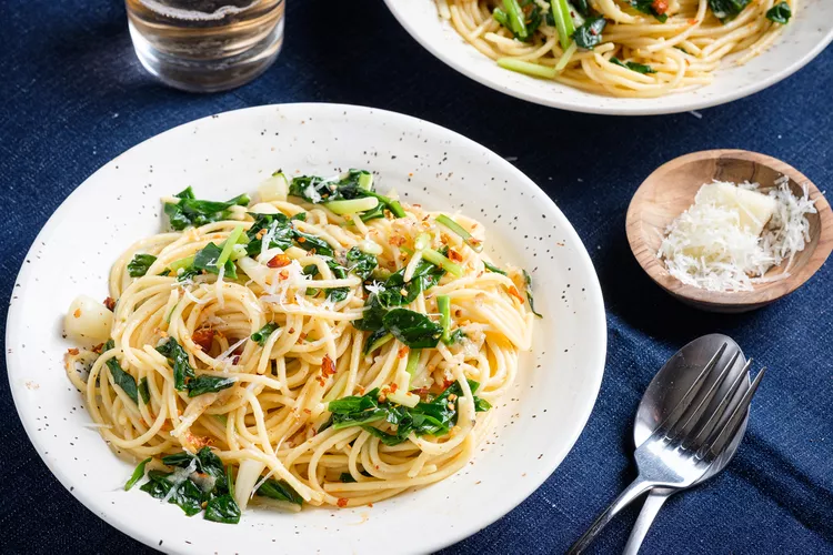 A white plate holds a spaghetti dish with a pair of forks sitting next to the plate on a blue table.