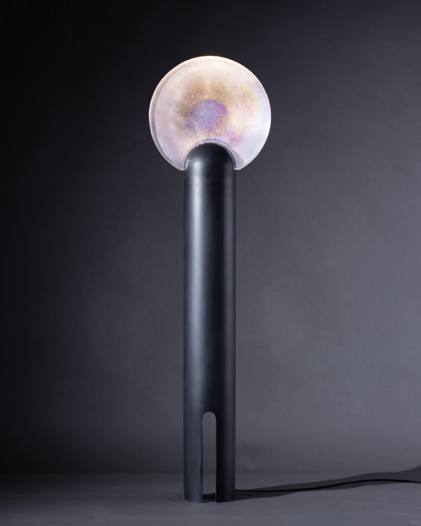 A round iridescent lamp sits on top of a long, wide black lamp post.
