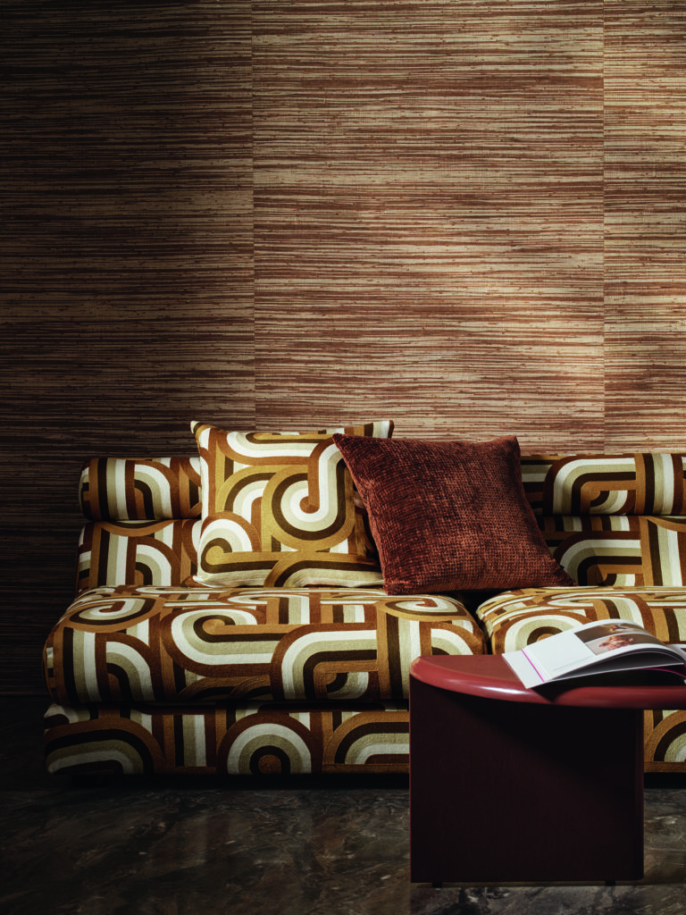 A yellow and brown patterned 70s style couch sits against a wood wall with a brown throw pillow on the couch.