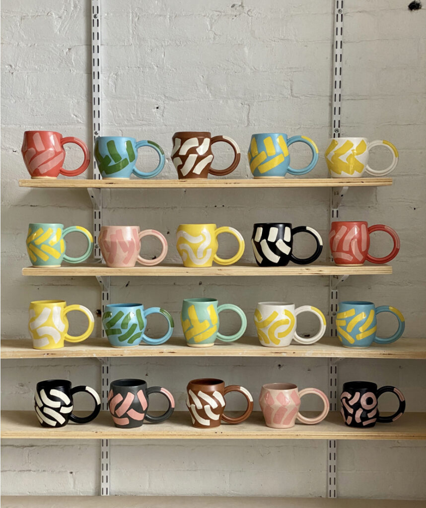Four yellow shelves hold various handcrafted ceramic colorful mugs.