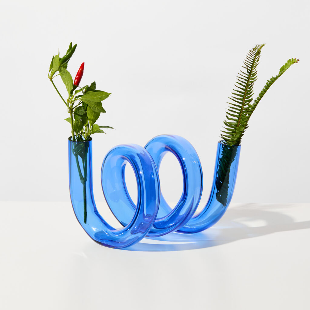 A blue swirly tube vase with plants stuck in end open tube end.
