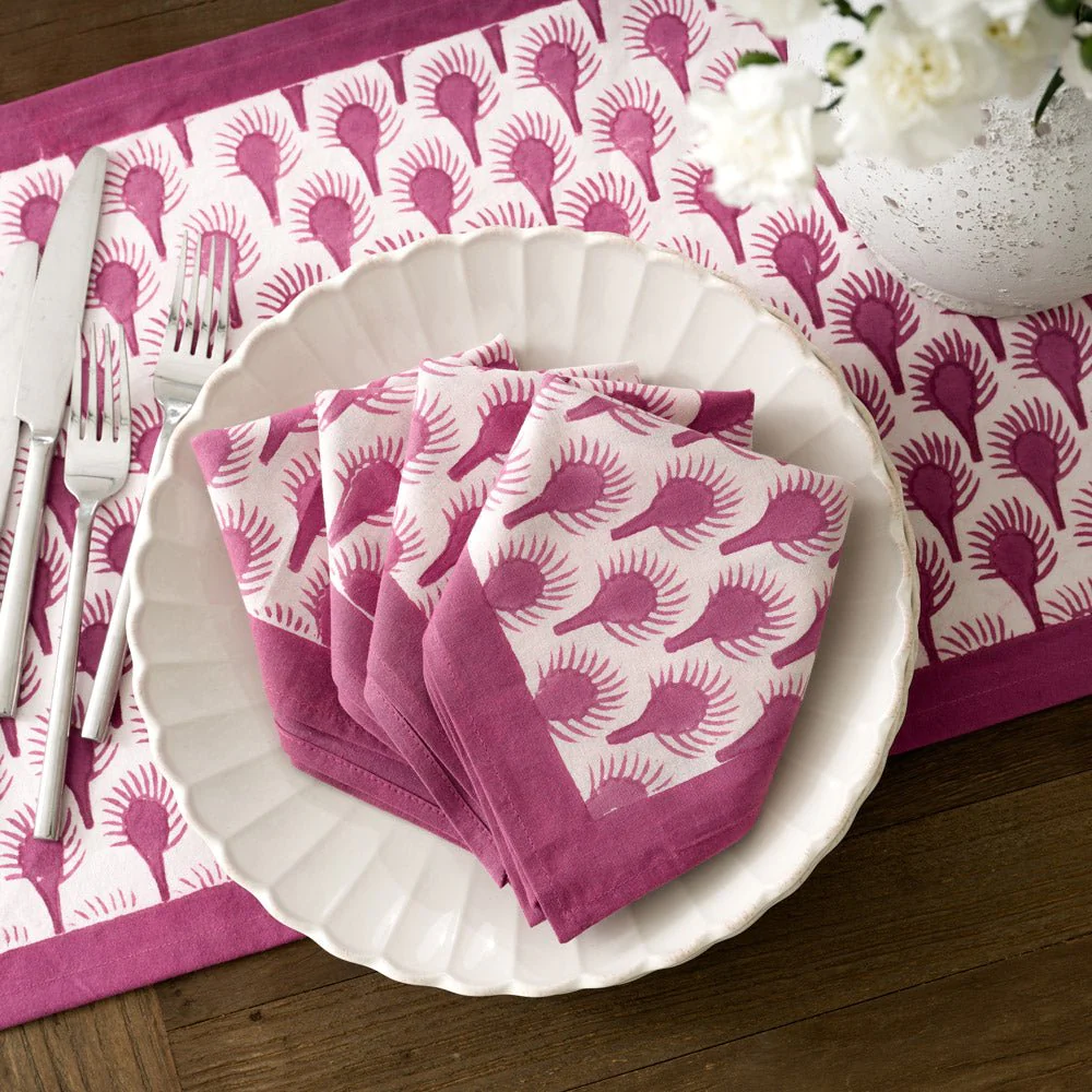 A white plate on top of a white and purple patterned table setting holds white and purple patterned napkins folded to a point.