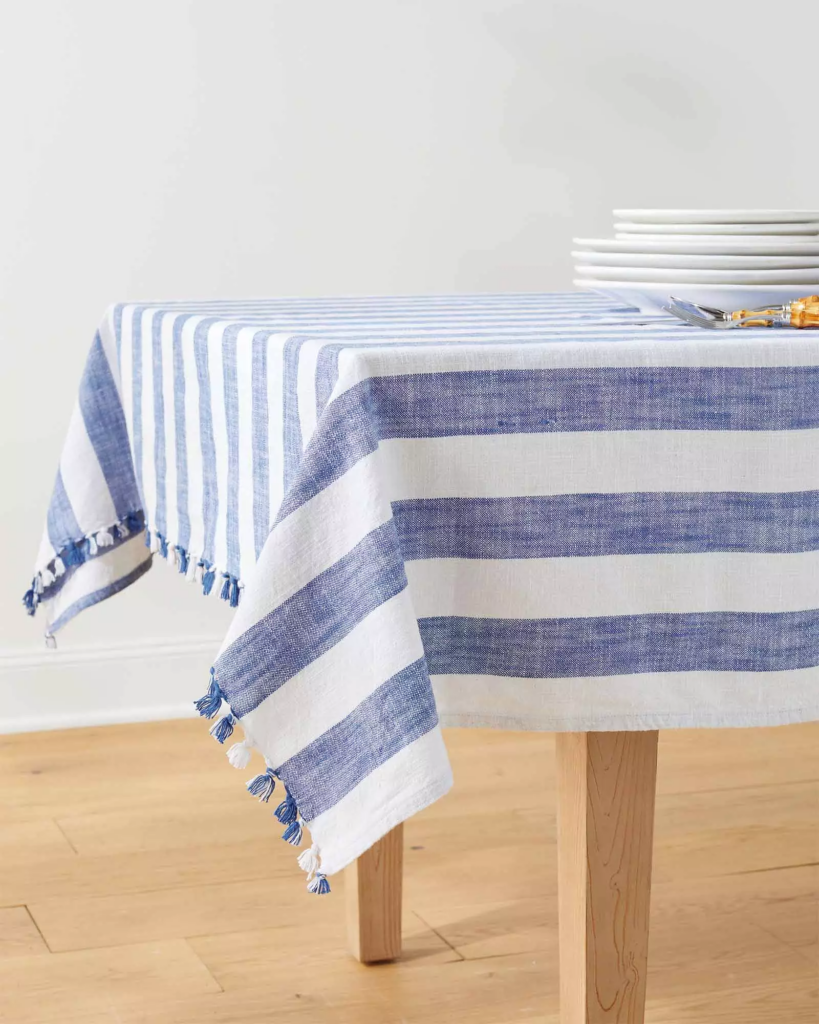 A blue striped tablecloth on a table ready for outdoors eating, featuring white tableware on top.