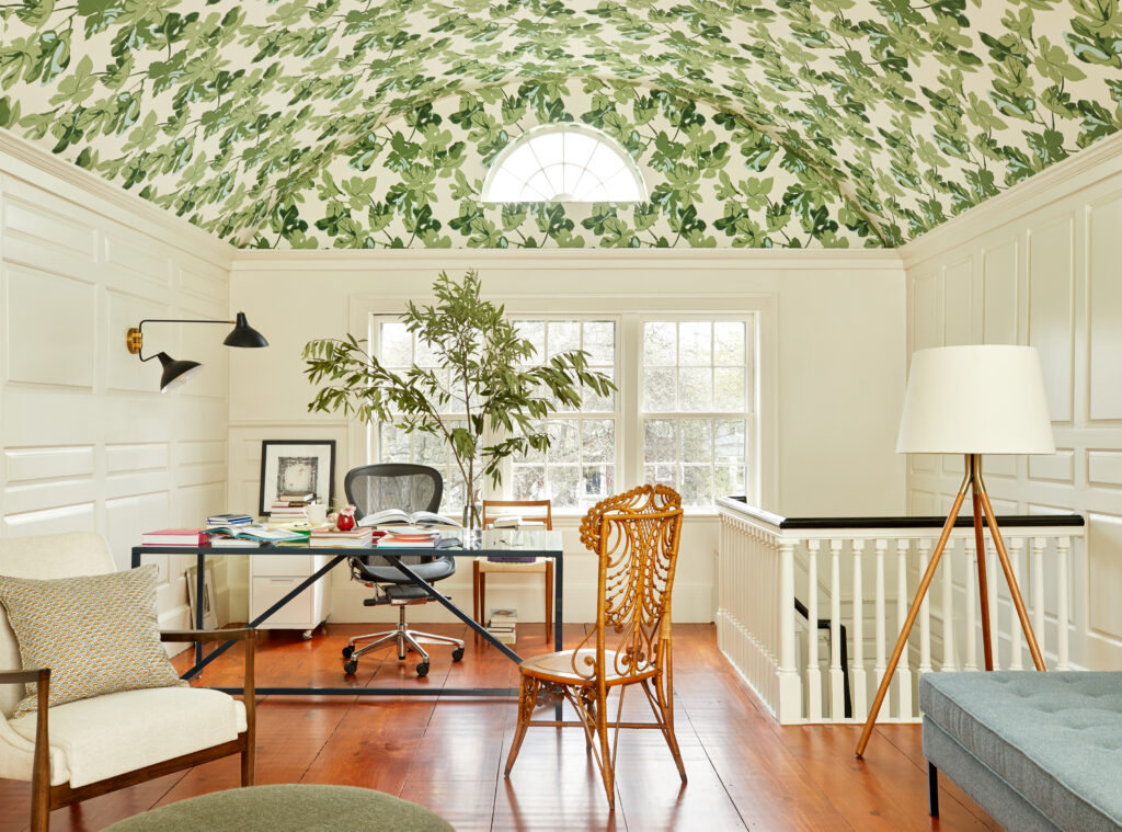 The upper floor of a home with wooden floors and a green pattern wallpaper ceiling with desks and chairs throughout the area.