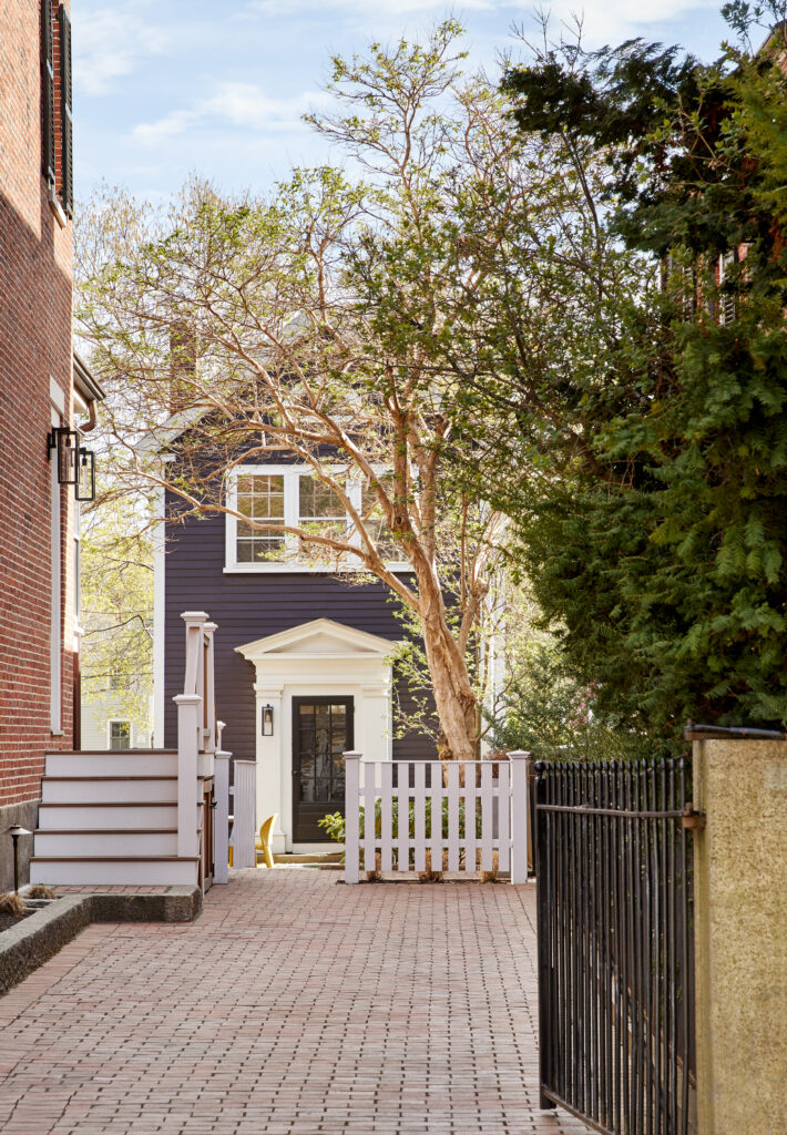 The exterior of a dark blue house designed by Colleen Simond with white trim and a white picket fence.
