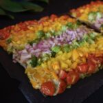 A flatbread pizza topped with veggies cut up in a rainbow design sits on a black countertop.
