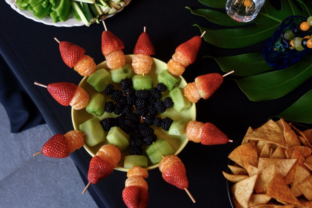 A ring of fruit skewers stacked from blackberries to grapes to oranges to strawberries, arranged in a circle in a bowl. 