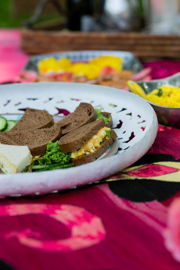 A white plate holds a selection of Curried Egg Sandwiches on top of a pink picnic blanket.