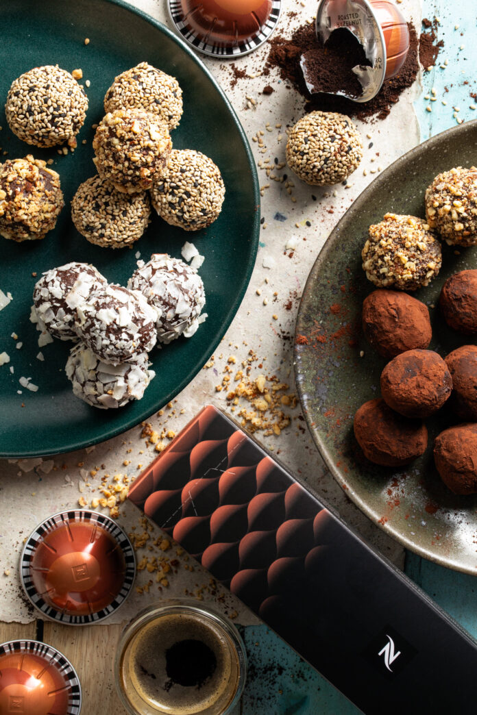 Two plates of mocha truffles coated in cocoa powder and nuts with nespresso pods and chocolate bars nearby.