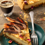A slice of Espresso Swirl Cheesecake sits on a green plate in front of the whole baked cheesecake and a shot of espresso.