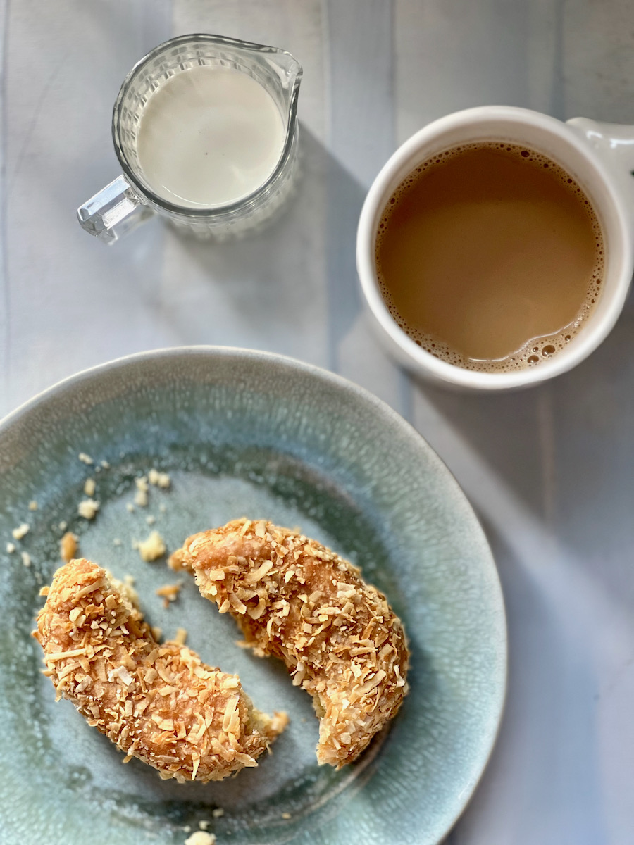 A coconut donut next to some coffee with milk 