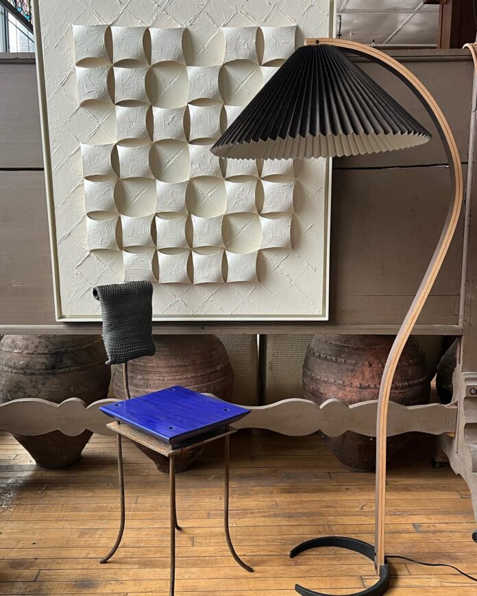 A blue chair sits beside a funky black lamp with a white board in the background.