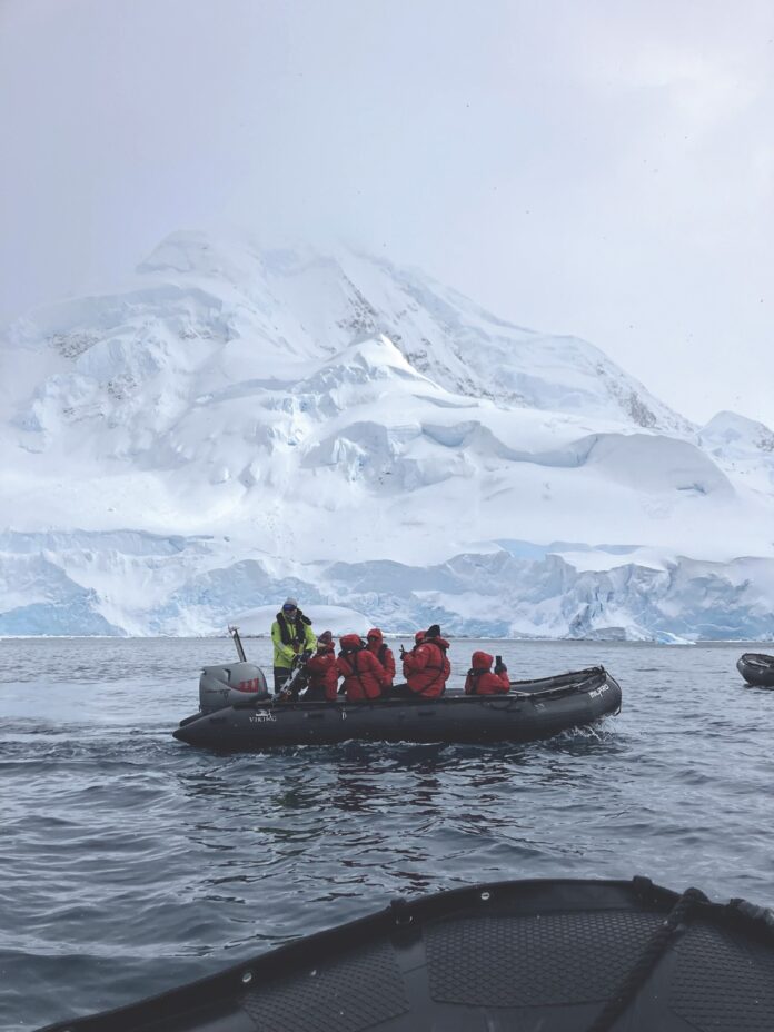 A small boat sails across the Antarctic ocean with a group of people in red jackets onboard.