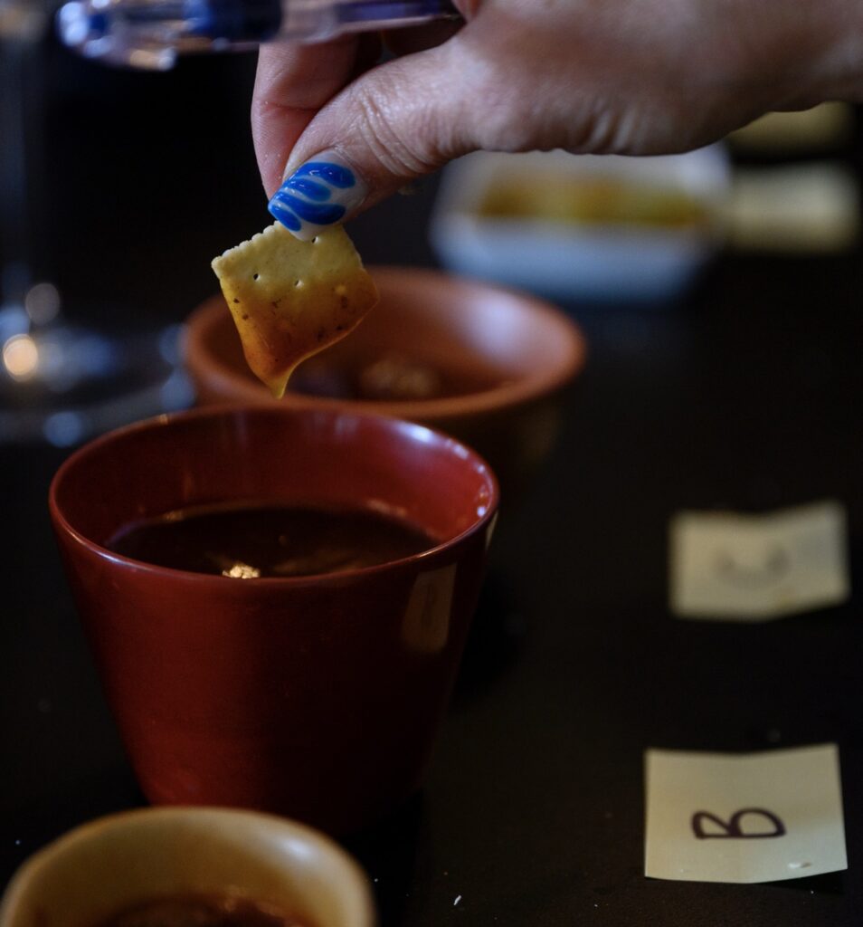 A person with blue nails dips a cracker into a container of hot sauce.
