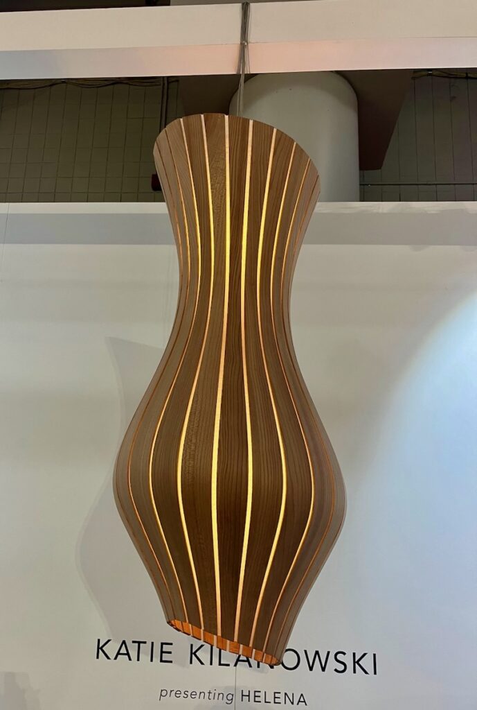 A long lamp made from wooden slits sits against a white background at New York Design Week.