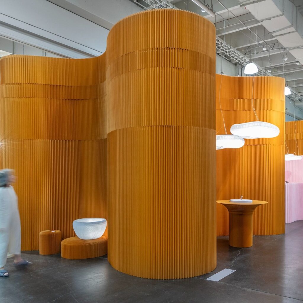 A brown four piece wall stands tall and has wooden seats sitting against the walls in the ICFF New York Design Week space.