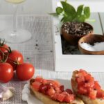 Bruschetta on a plate beside some heirloom tomatoes