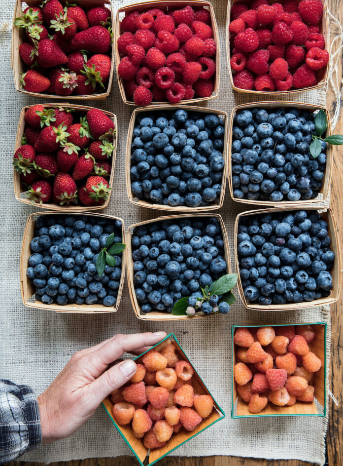 Blueberries, strawberries, and raspberries on a farm table.