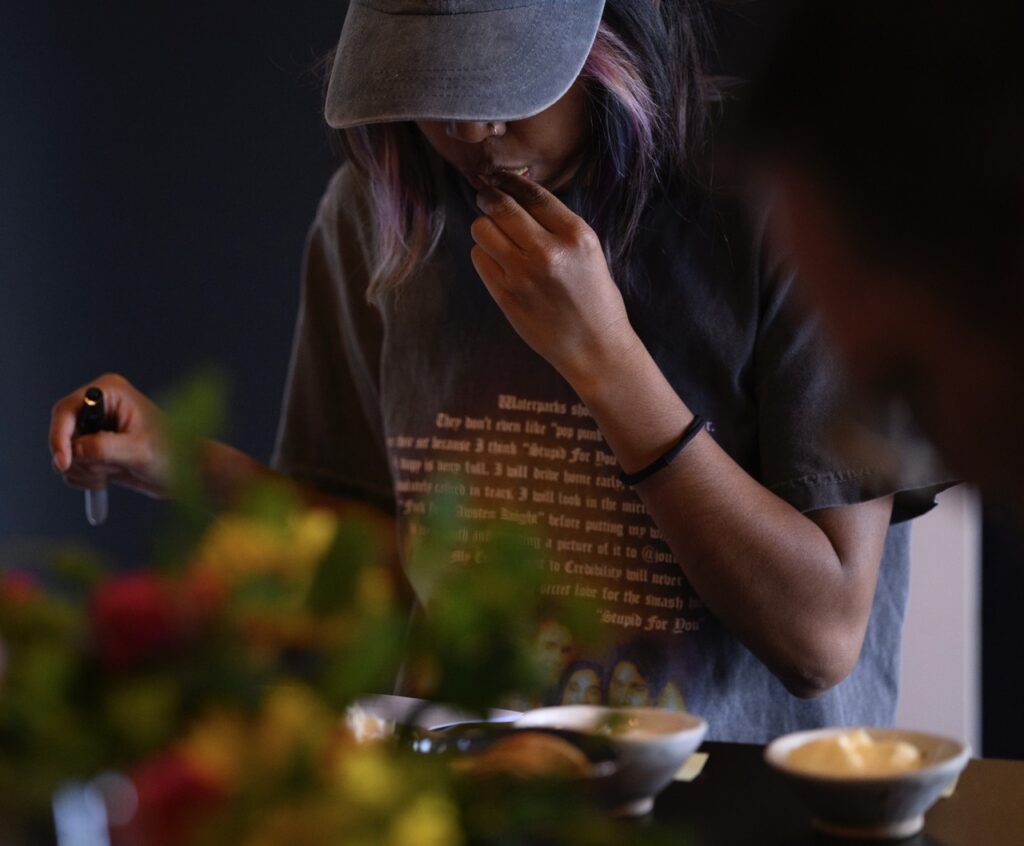 A person in a baseball hat munches on a small cracker while looking down at the condiments.