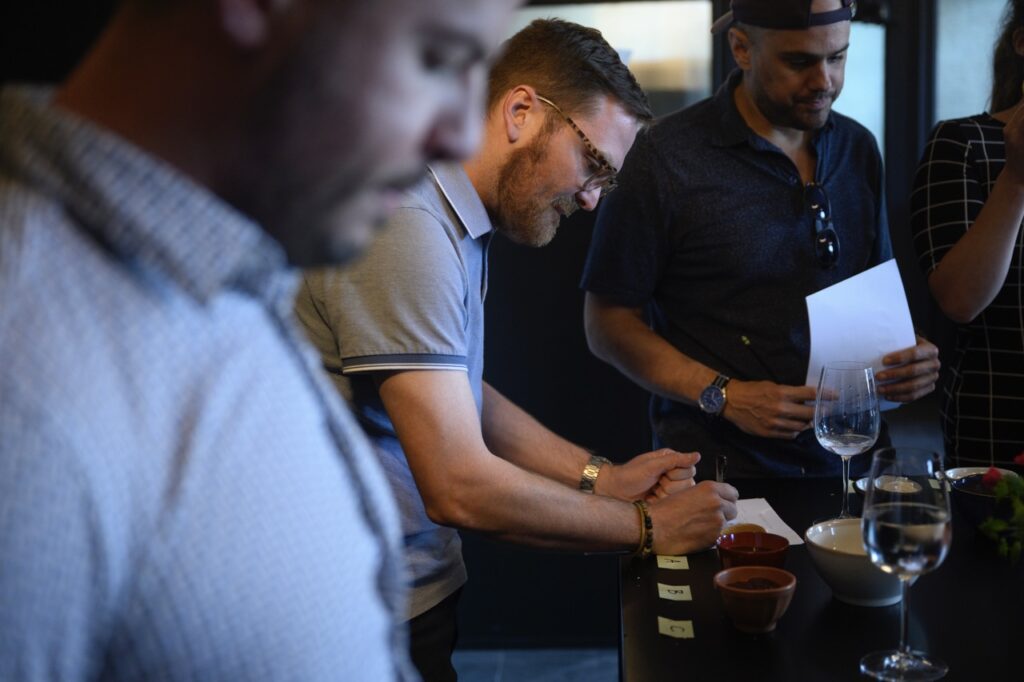 A man looks down on a table of condiments in thought as others stand around him.