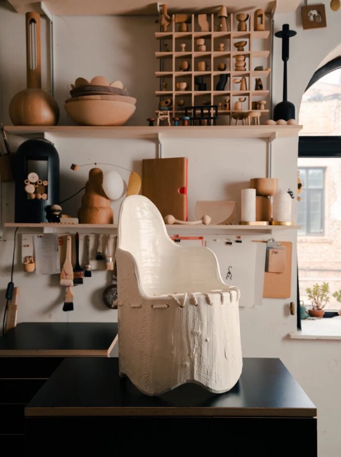 The inside of Assembly Line Design Shop in Boerum Hill featuring a white chair on a black display table and wood shelves with wood products in the background.