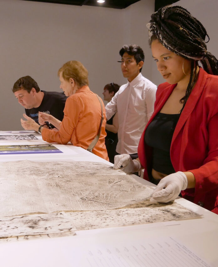 A woman peruses a set of flatfiles on a white table at the Kansas City Art Institute