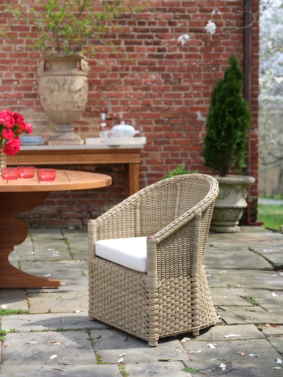 A larger outdoor brown wicker chair with a white cousin sits by a brown table.