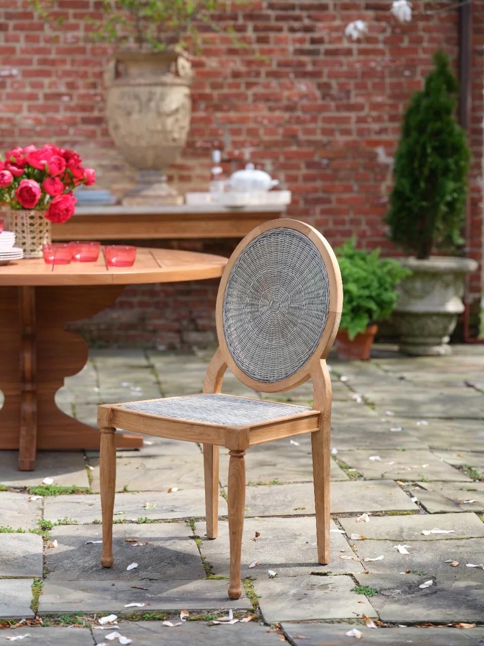 A Bunny Williams Louis chair sits outside in front of a brown table.